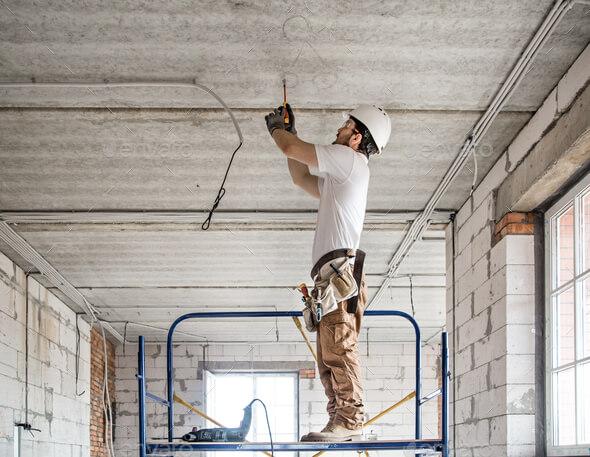 Electrician installer with a tool in his hands, working with cable on the construction site. Repair and handyman concept. House and house reconstruction.